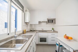 Une cuisine moderne équipée d’un évier en acier inoxydable, d’un four à micro-ondes, d’un four encastré et d’une fenêtre avec des stores.