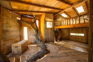 A rustic cabin interior with wooden walls, a slanted roof, and a large tree branch as a central feature.