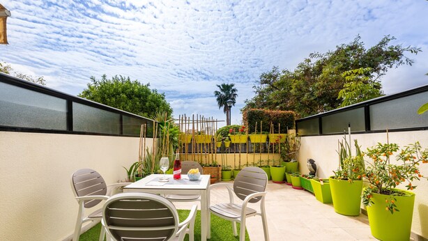 Eine Terrass mit Tisch und Stühlen, umgeben von Topfpflanzen und Blick auf einen Garten.