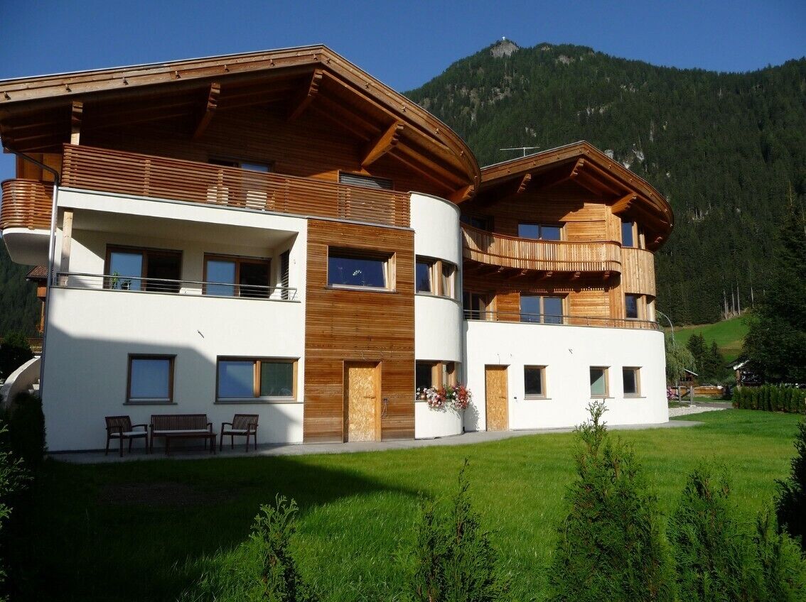 Un immeuble moderne à plusieurs étages, doté de balcons, d’un toit plat et surplombant un paysage montagneux.