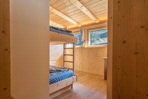 Ein Schlafraum mit Etagenbetten, einer Holzbalkendecke und einem Fenster mit Blick auf eine verschneite Landschaft.
