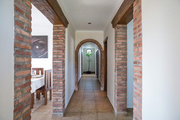 A hallway with brick columns, a dining area with a table and chairs, and a plant in the distance.