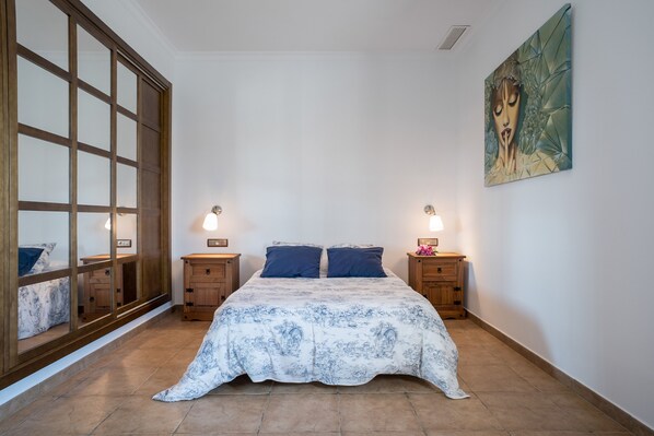 A bedroom with a bed, nightstands, a mirror, and a painting on the wall.