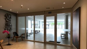 A modern reception area with glass doors, a seating area with chairs, a vase with flowers, and a sign indicating the exit. - Studio Sky Centro (São Paulo)