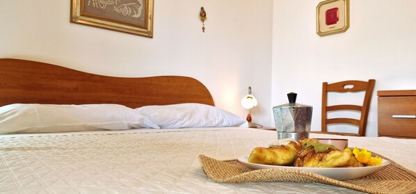 A bed with white linens, a wooden headboard, a bedside table with a lamp, a chair, and a plate of food on the bed. - Villa 'Paradiso' with Private Pool, Wi-Fi and Air Conditioning (Alcamo)