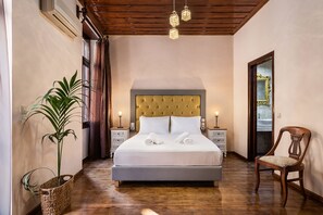 A bedroom with a large bed, bedside tables, a potted plant, and a wooden chair. - Old Town Suites (Chania)
