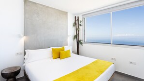 A modern bedroom with a large bed, a view of the ocean, and a minimalist design.