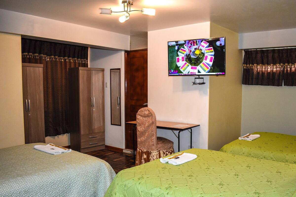 A hotel room with two beds, a desk, a chair, and a TV on the wall.