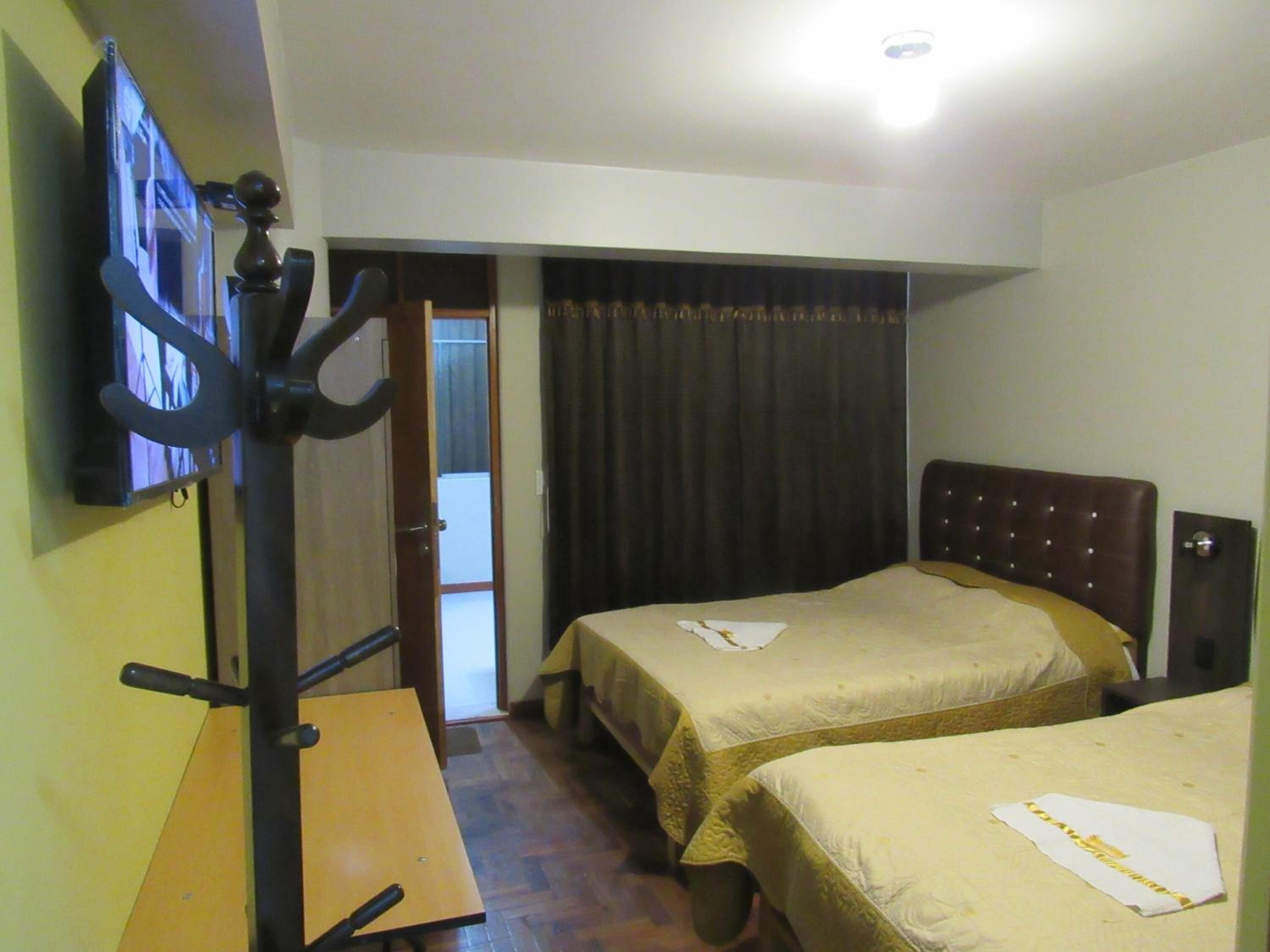 A hotel room with two beds, a desk, a television, and a door leading to a balcony.