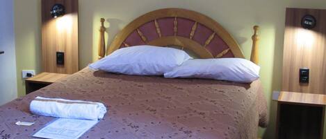 Una cama bien hecha con una colcha estampada, dos mesitas de noche con lámparas y un cabecero de madera.