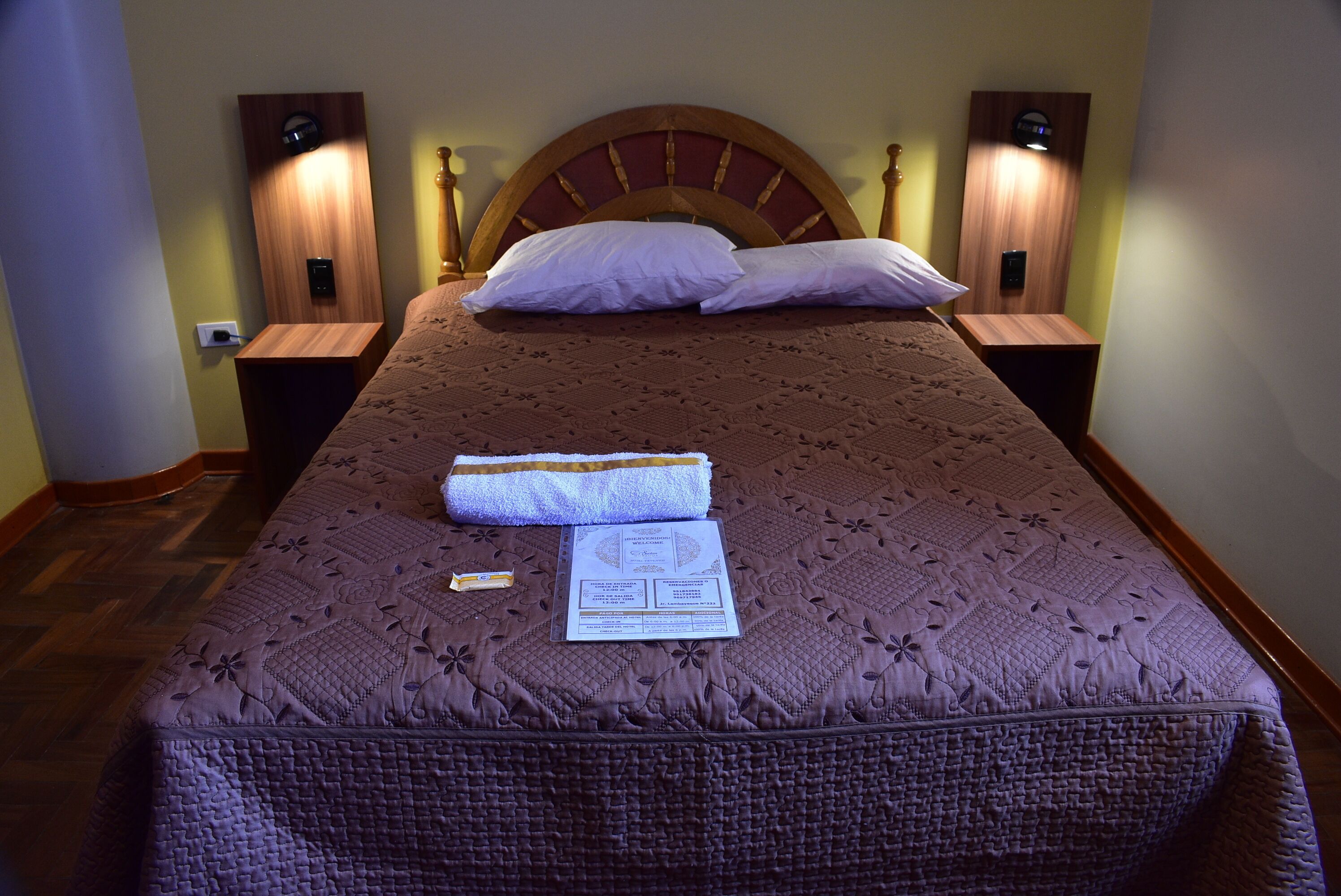 A neatly made bed with a headboard, two bedside tables with lamps, and a visible power outlet on the wall.