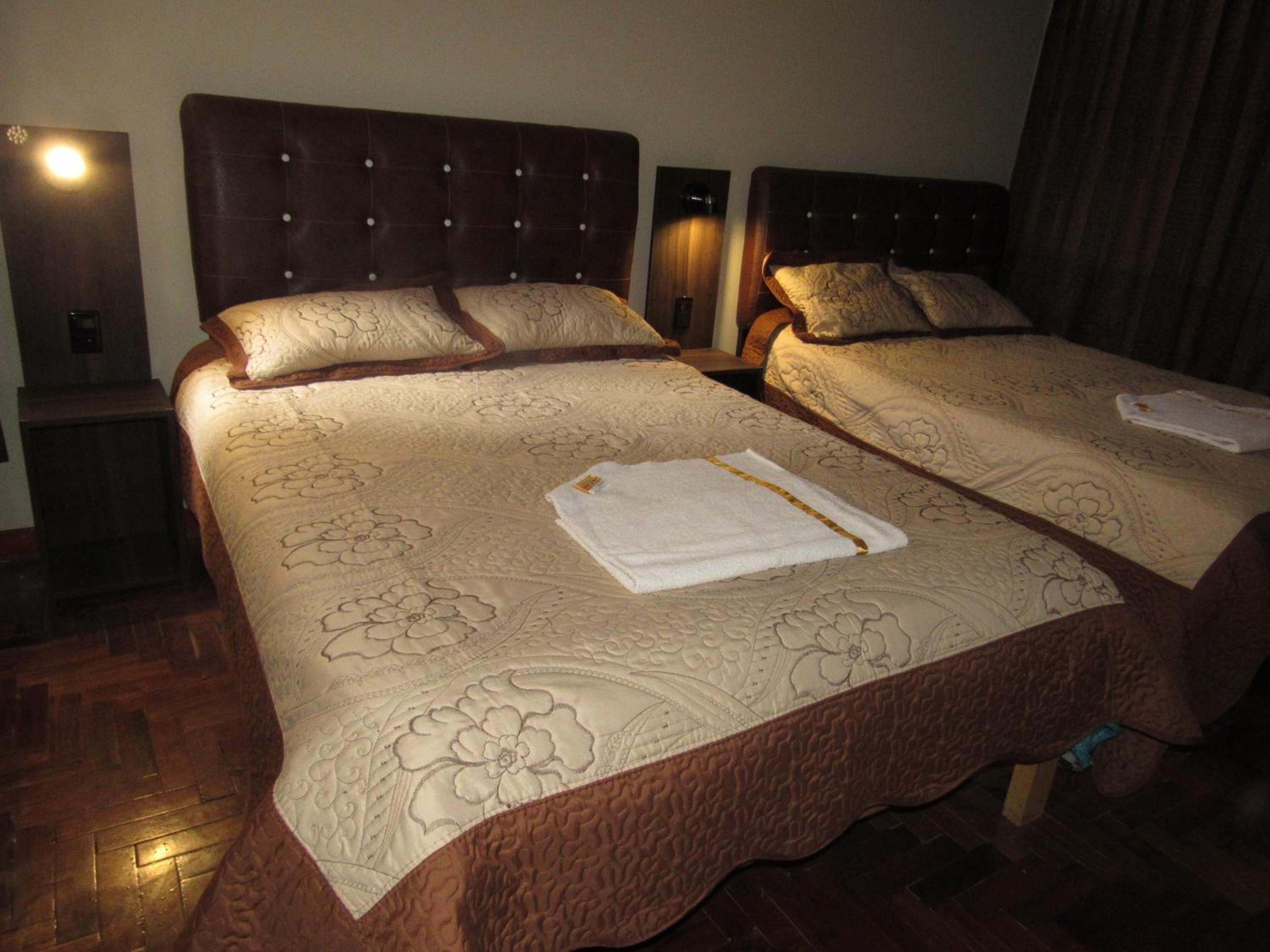 Two double beds with floral-patterned bedding, a wooden headboard, and a nightstand with a lamp.
