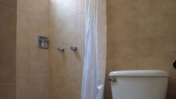 Un baño con inodoro, ducha con cortina blanca y ventana.