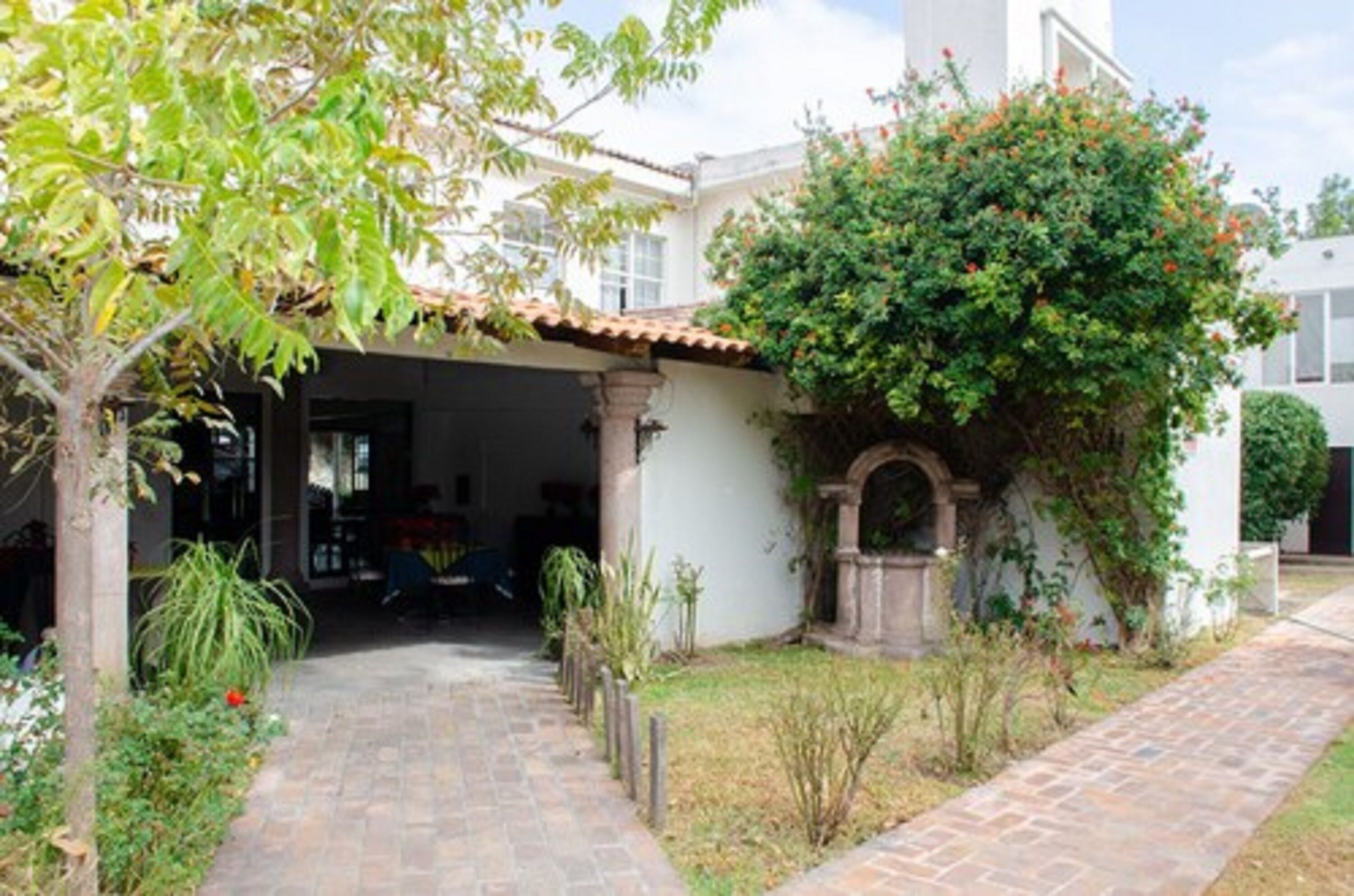 Un patio cubierto con un sendero de piedra que conduce a la entrada de un edificio, rodeado de follaje y un pequeño arco.