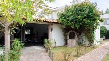 Un patio cubierto con un sendero de piedra que conduce a la entrada de un edificio, rodeado de follaje y un pequeño arco.