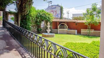 Entrada de hotel con un letrero, una fuente y un jardín bien cuidado.