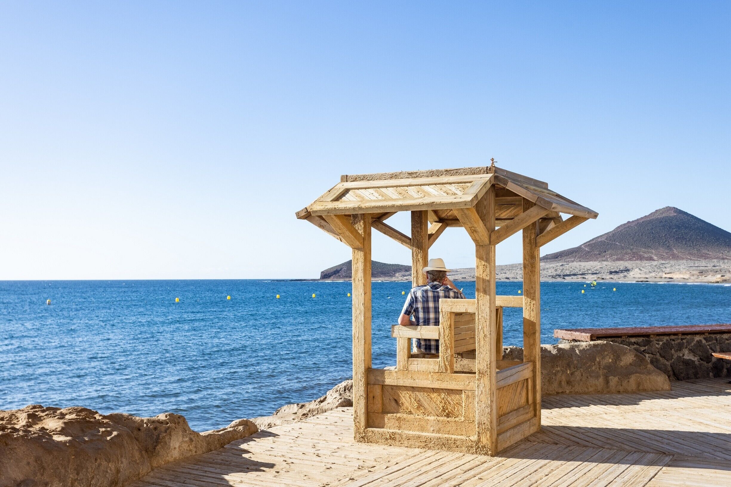 Ein hölzerner Pavillon mit einer Person darin, die einen Blick auf einen Strand mit einem Berg im Hintergrund hat.