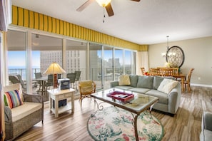 Relax in a spacious living room with a sofa, armchairs, and dining table, leading to a balcony with city views.