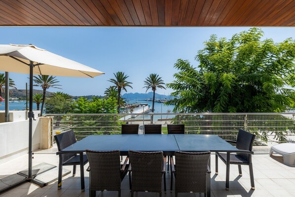 A terrace with a table and chairs, a view of the sea, and palm trees. - Olympo Holiday Apartment on the Seafront (Puerto Pollensa)