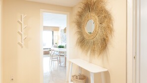 Un couloir avec une console blanche, un miroir en osier et une plante fixée au mur.
