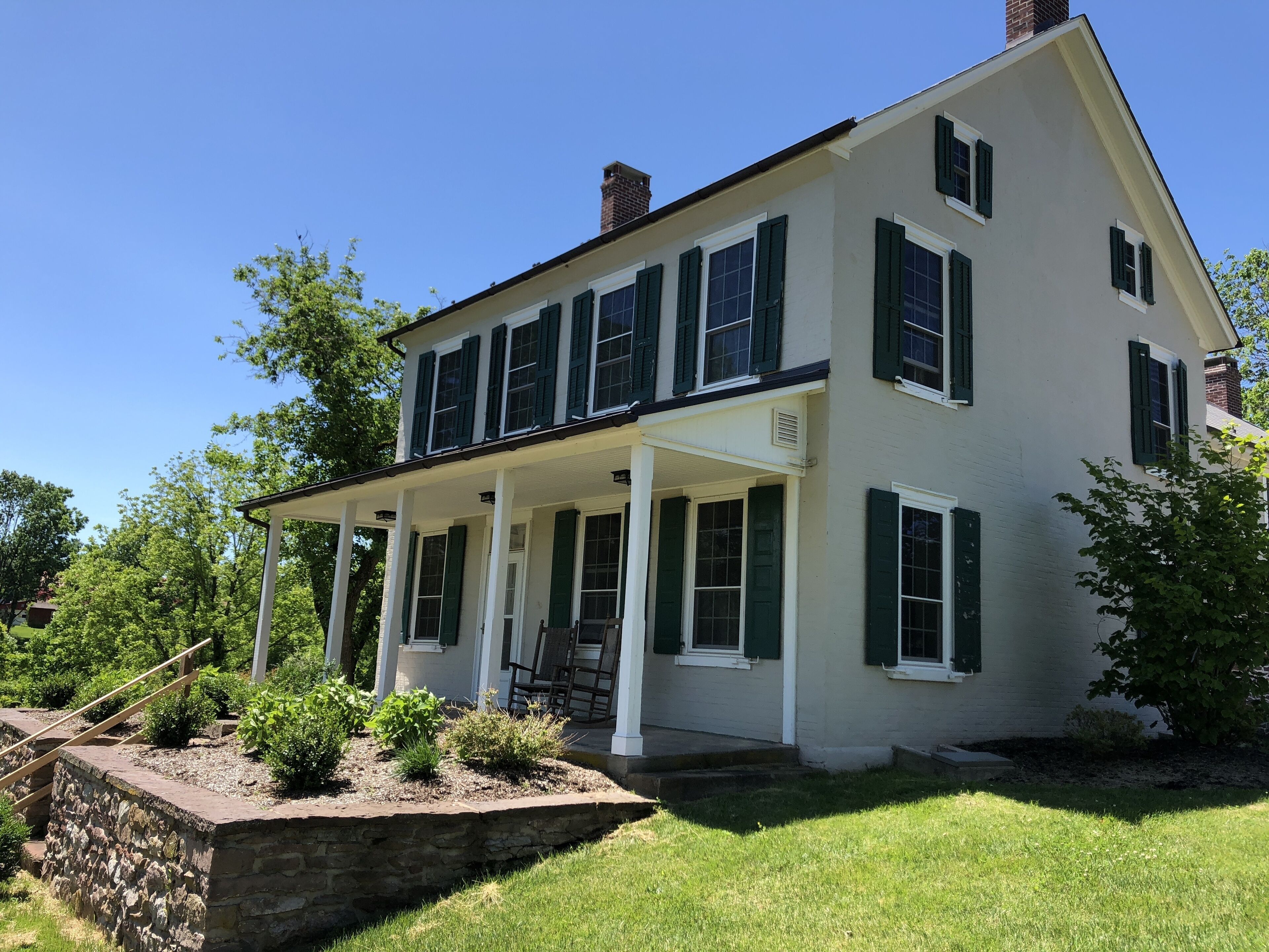 A two-story house with a porch, stone retaining wall, and a well-maintained lawn.