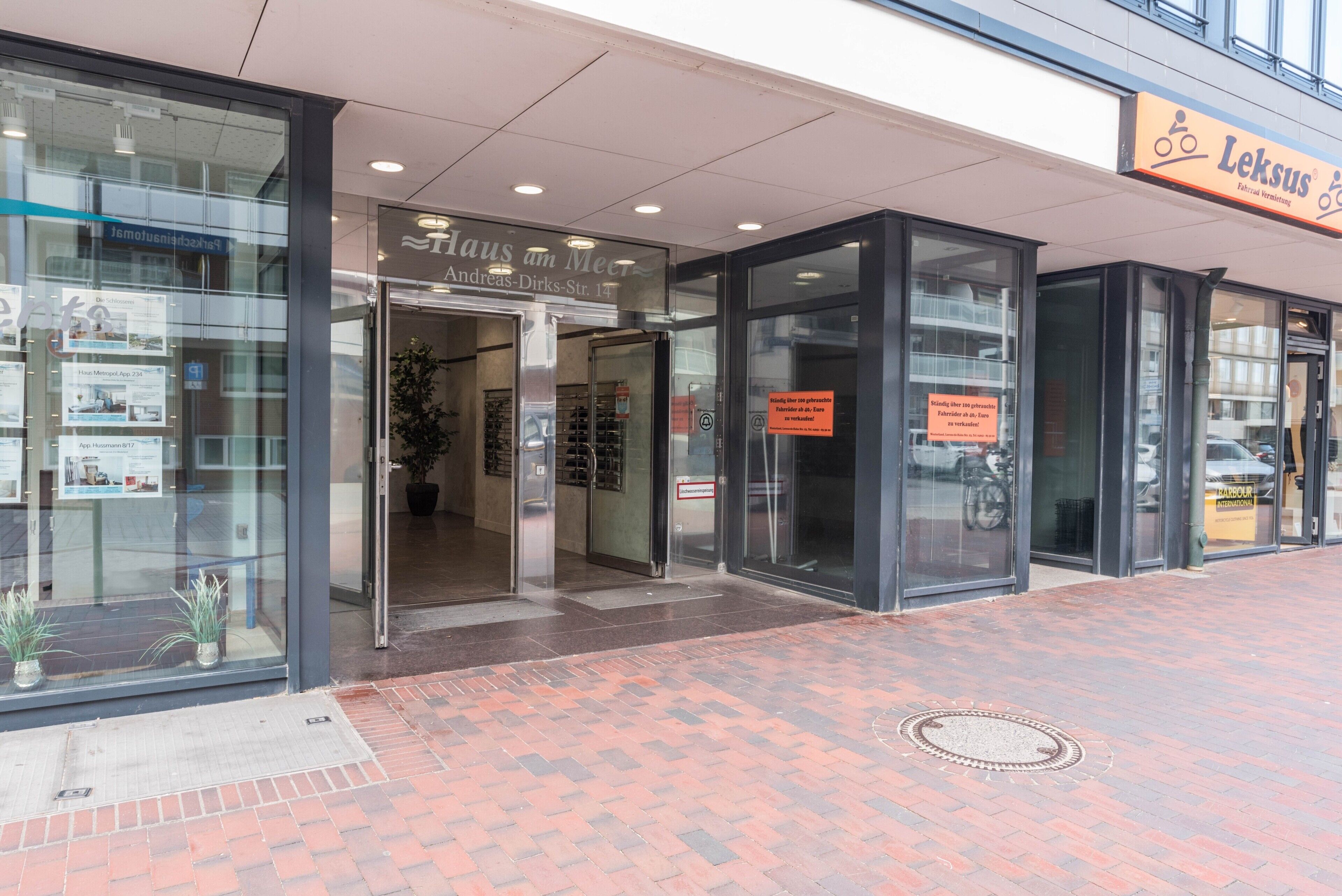 A building entrance with glass doors, a sign for 'Haus am Meer,' and a 'Leksus' sign above.