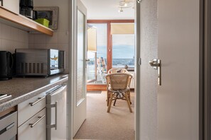 A kitchen with a microwave, a coffee maker, and a wicker chair in a room with a view.