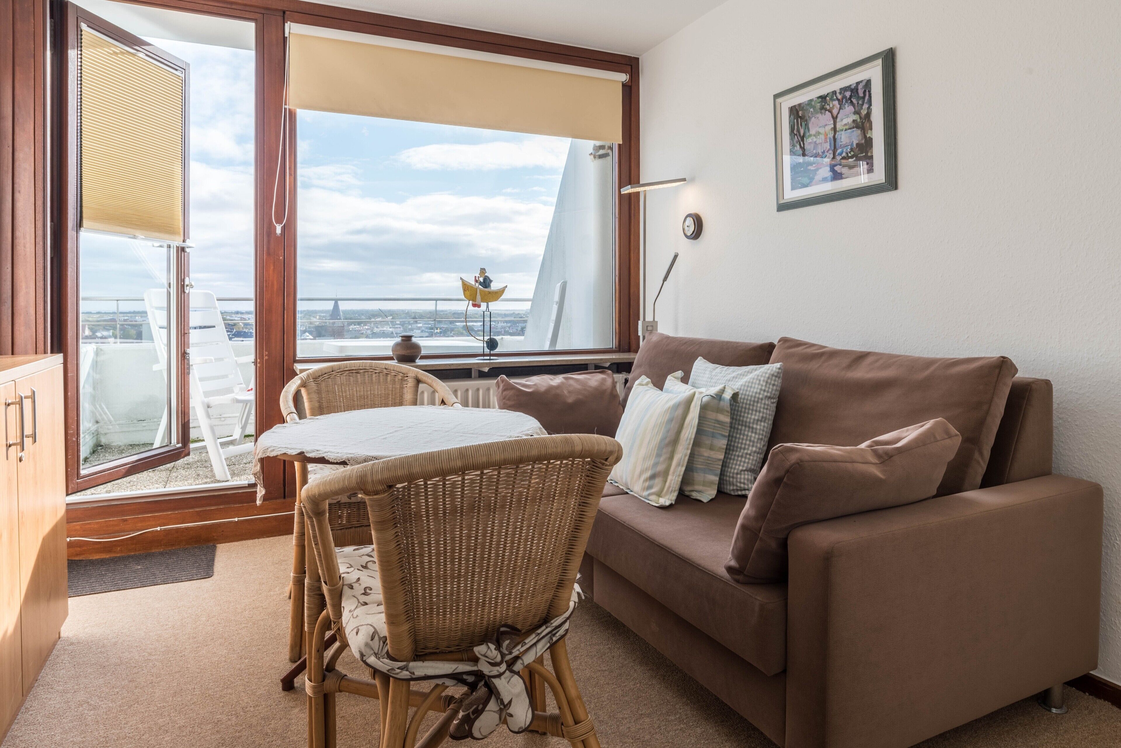Ein Wohnzimmer mit einer Couch, einem Korbsessel, einem Tisch und Blick auf eine Brücke durch ein Fenster.