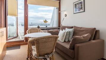 Ein Wohnzimmer mit einer Couch, einem Korbsessel, einem Tisch und Blick auf eine Brücke durch ein Fenster.
