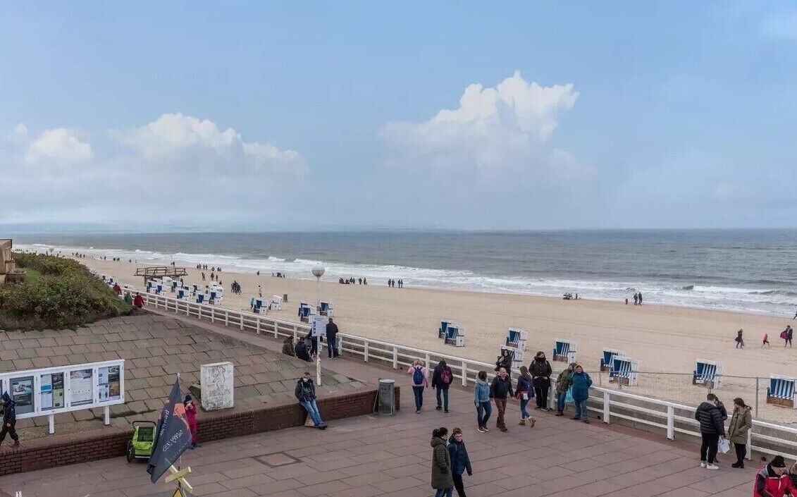 A beach with people, a boardwalk, and a view of the ocean.