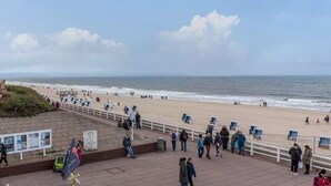 Uma praia com pessoas, um calçadão e vista para o oceano.