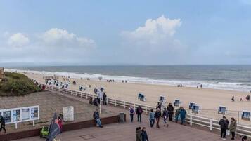 A beach with people, a boardwalk, and a view of the ocean.