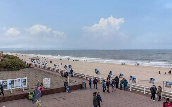A beach with people, a boardwalk, and a view of the ocean.