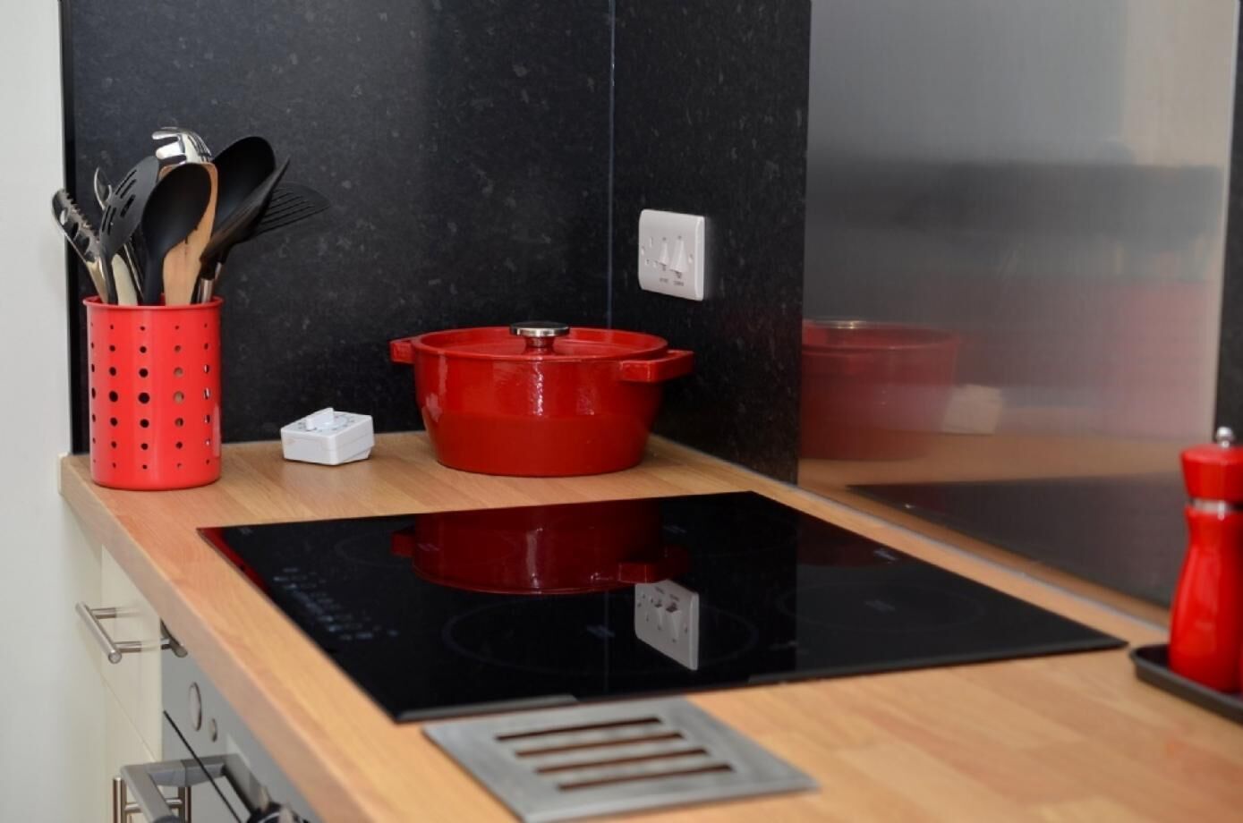 Una cocina con una placa de inducción negra, una olla roja y un portalapices rojo.