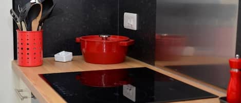 Una cocina con una placa de inducción negra, una olla roja y un portalapices rojo.