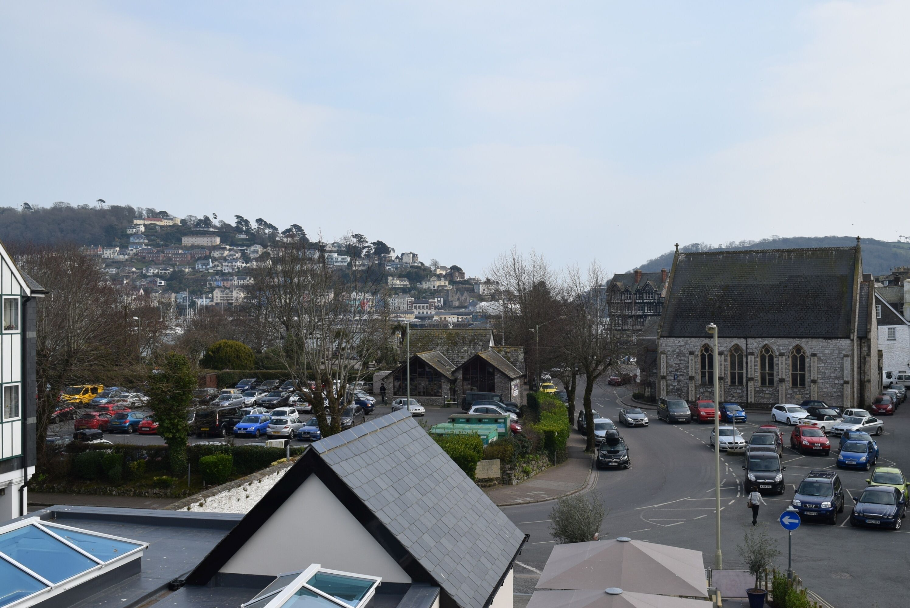 A residential street with parked cars, a church, and houses on a hillside.