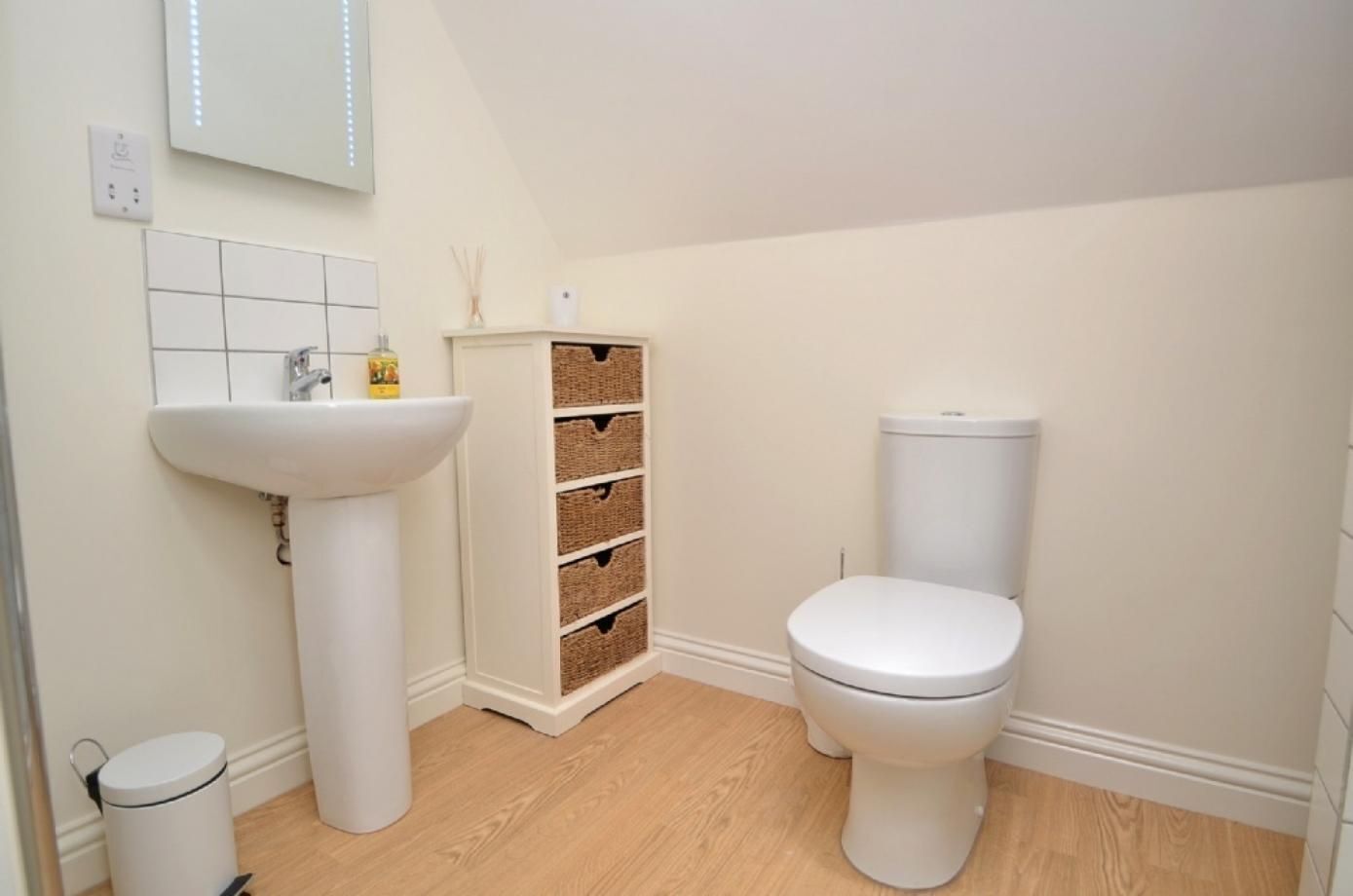 A bathroom with a pedestal sink, a toilet, and a storage unit with baskets.