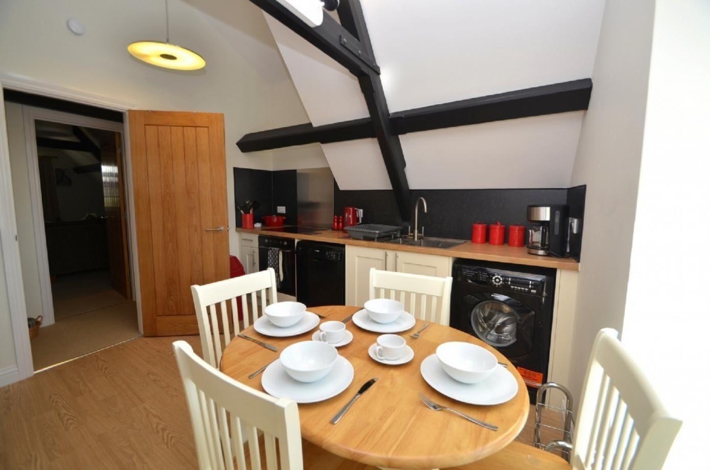 A compact kitchen with a dining area, featuring a round wooden table set for four, white chairs, and a black and white color scheme.