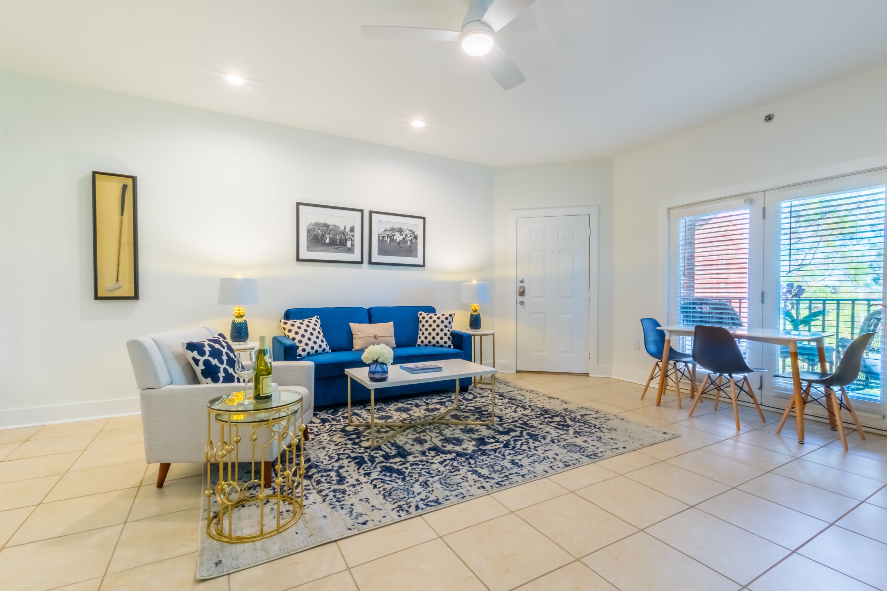 A living room with a sofa, coffee table, and chairs, a patterned rug, and a door leading to a balcony.