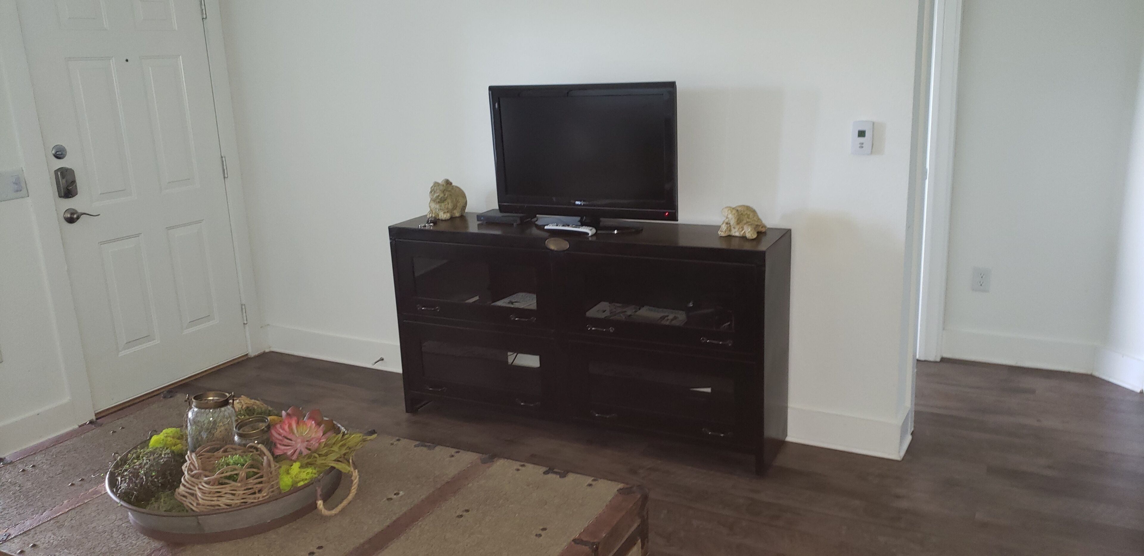 En stue med et sort multimediemøbel, et fjernsyn og to dekorative genstande ovenpå.