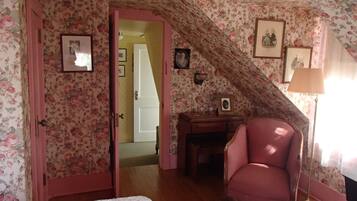 A bedroom with floral wallpaper, a pink chair, a desk, and a bed.