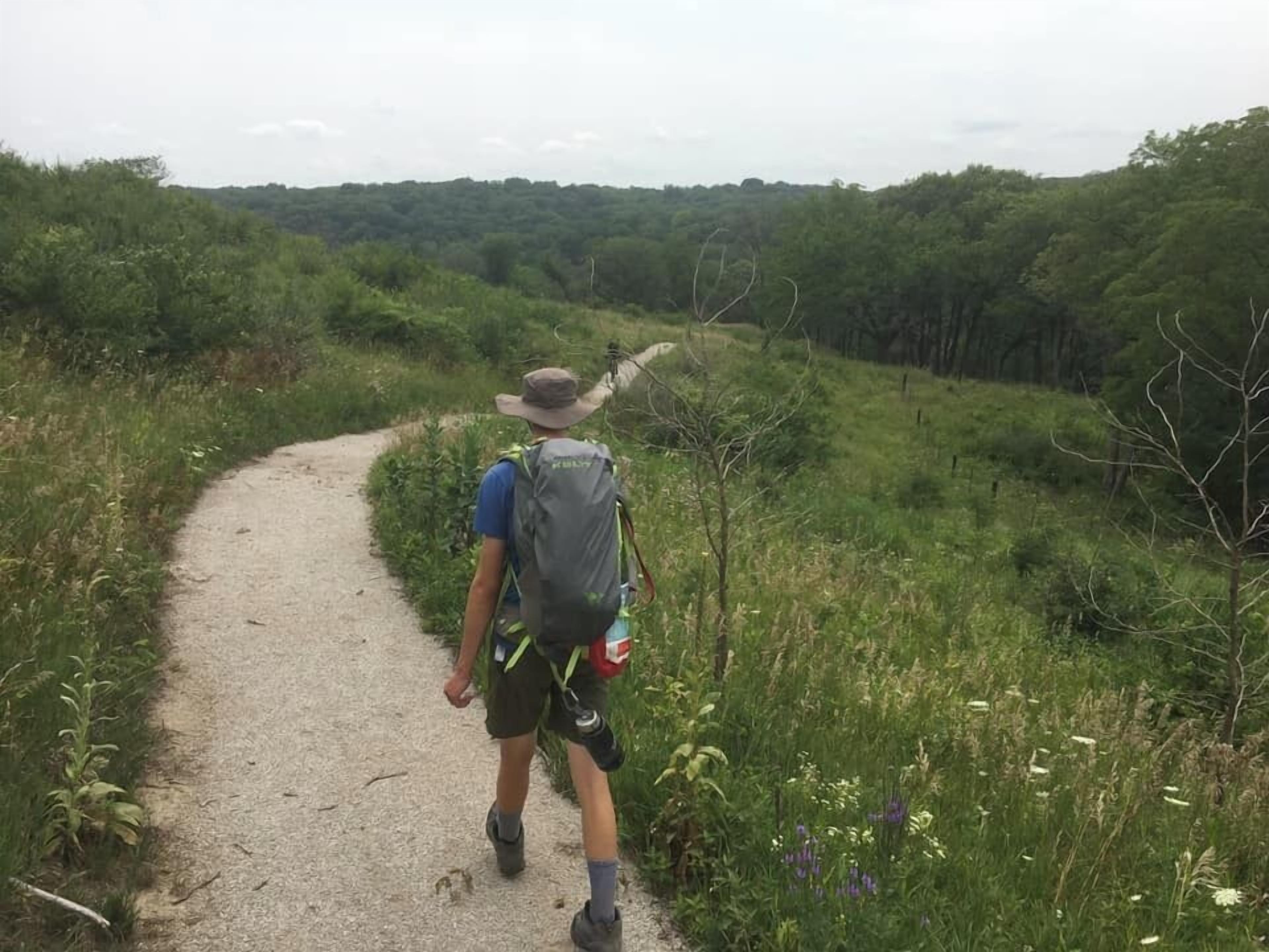 Une personne marchant sur un sentier de terre, entourée de verdure.