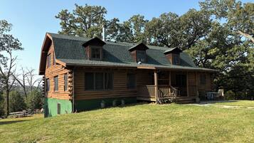 A log cabin with a porch, multiple windows, and a chimney.