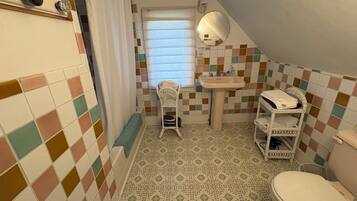 Une petite salle de bain carrelée, équipée de toilettes, d’un lavabo et d’une chaise.