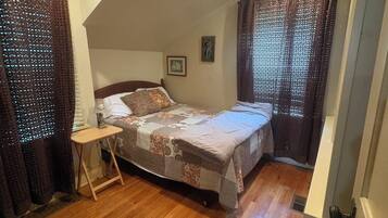 Un dormitorio con techo inclinado, una cama, una mesita de noche y un ventanal con cortinas.