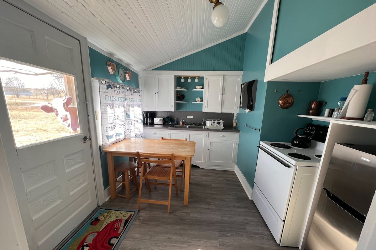 A compact kitchen with white cabinets, a wooden dining table, and a stainless steel refrigerator.