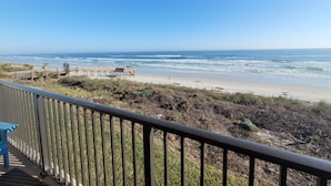 Blick auf einen Strand von einem Balkon mit einer Holzterrasse und einem Geländer.