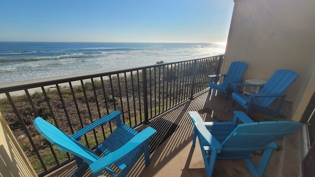 Ein Balkon mit blauen Adirondack-Stühlen, einem kleinen Tisch und Blick auf das Meer.