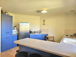 A modern kitchen with a central island, built-in cabinets, a microwave, a coffee maker, and a kettle.