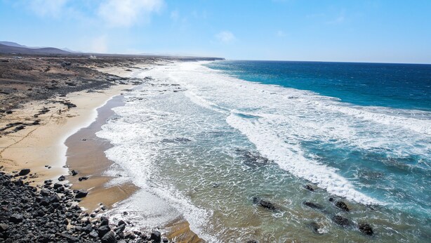 Eine Küstenlandschaft mit Sandstrand, felsigem Ufer und blauem Himmel.